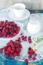 Fresh raspberries on a plate, a white cup, chamomile and a jug of milk on a blue wooden background in a rustic style. Still life. Royalty Free Stock Photo