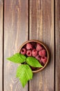 Fresh raspberry red berries with green leaves in bowl on wooden table Royalty Free Stock Photo