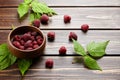 Fresh raspberry red berries with green leaves in bowl on wooden table Royalty Free Stock Photo