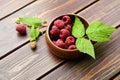 Fresh raspberry red berries with green leaves in bowl on wooden table Royalty Free Stock Photo