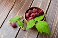 Fresh raspberry red berries with green leaves in bowl on wooden table Royalty Free Stock Photo