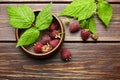 Fresh raspberry red berries with green leaves in bowl on wooden table Royalty Free Stock Photo