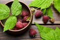 Fresh raspberry red berries with green leaves in bowl on wooden table Royalty Free Stock Photo