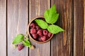 Fresh raspberry red berries with green leaves in bowl on wooden table Royalty Free Stock Photo