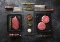 Fresh raw beef fillet steak and mince burgers in vacuum tray with cleavers and rosemary on black background with rosemary