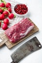 Fresh raw beef tenderloin with seasonings and rosemary, a whole uncut piece, on white stone background