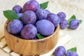 Fresh raw blue and violet plums in wooden bowl with green leaves on light paper background. Royalty Free Stock Photo