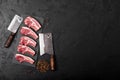 Fresh raw butchers lamb beef cutlets on stone board with vintage hatchets on black stone background. Space for text