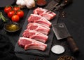 Fresh raw butchers lamb beef cutlets on stone board with vintage meat fork and knife and hatchet on black background.Salt, pepper Royalty Free Stock Photo