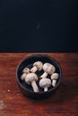 Fresh raw champignon mushrooms in black bowl on wooden background. Autumn harvest, seasonal organic food, healhty eating. Copy