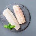 Fresh raw cod fillet with basil on a stone plate, top view, square