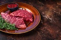 Fresh Raw denver or top blade meat steak on a rustic plate with thyme. Dark background. Top view. Copy space