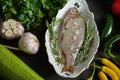 Fresh raw dorada fish in a white dish with a set of vegetables on a black table Royalty Free Stock Photo