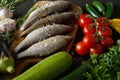 Fresh raw dorada fish on a wooden board with a set of vegetables on a black table Royalty Free Stock Photo