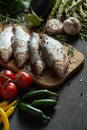 Fresh raw dorada fish on a wooden board with a set of vegetables on a black table Royalty Free Stock Photo