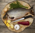 Fresh raw fish carp caught lying on a wooden stump with a knife and slices of lemon and with salt dill. Live fish crucian Carassiu