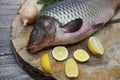 Fresh raw fish carp caught lying on a wooden stump with a knife and slices of lemon and with salt dill. Live fish crucian Carassiu