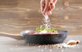 Fresh raw flank steak in the pan. The woman`s hand adds salt to the meat. Ingredients are spices, rosemirine various sprouts and