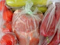 Fresh raw foods in plastic bags just bought by weight: a piece of pork meat, two zucchini, few red tomatoes and red peppers