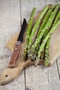 Fresh raw garden asparagus and knife closeup on cutting board on rustic wooden table background. Green spring vegetables Royalty Free Stock Photo