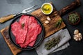 Fresh raw meat beef steaks. Beef tenderloin in cast iron pan on wooden board, spices, herbs, oil on slate gray background. Food ba Royalty Free Stock Photo