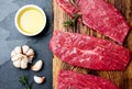 Fresh raw meat beef steaks. Beef tenderloin on wooden board, spices, herbs, oil on slate gray background. Food cooking background Royalty Free Stock Photo