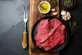 Fresh raw meat beef steaks. Beef tenderloin in cast iron pan on wooden board, spices, herbs, oil on slate gray background. Food ba Royalty Free Stock Photo