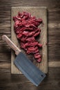 Fresh raw meat cut into pieces for cooking beef stroganoff lies on a wooden cutting board with a kitchen cleaver on a background Royalty Free Stock Photo