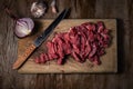 Fresh raw meat cut into pieces in the process of cooking beef stroganoff lies on a wooden cutting board with a kitchen knife, Royalty Free Stock Photo