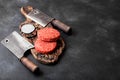 Fresh raw minced homemade farmers grill beef burgers on vintage chopping board with spices and herbs and meat hatchets on black