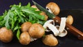 Fresh raw mushrooms brown champignons and green arugula on a dar