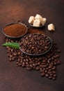 Fresh raw organic coffee beans with ground powder and cane sugar cubes with coffee trea leaf on brown background