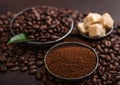 Fresh raw organic coffee beans with ground powder and cane sugar cubes with coffee trea leaf on brown background