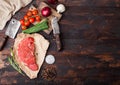 Fresh raw organic slice of braising steak fillet on butchers paper with fork and knife on dark wooden background. Red onion, Royalty Free Stock Photo