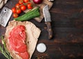 Fresh raw organic slice of braising steak fillet on butchers paper with fork and knife on dark wooden background. Red onion, Royalty Free Stock Photo