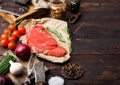 Fresh raw organic slice of braising steak fillet on butchers paper with fork and knife on dark wooden background. Red onion, Royalty Free Stock Photo