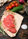 Fresh raw organic slice of braising steak fillet on butchers paper with fork and knife on dark wooden background. Red onion, Royalty Free Stock Photo