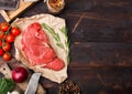 Fresh raw organic slice of braising steak fillet on butchers paper with fork and knife on dark wooden background. Red onion, Royalty Free Stock Photo