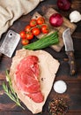 Fresh raw organic slice of braising steak fillet on butchers paper with fork and knife on dark wooden background. Red onion, Royalty Free Stock Photo