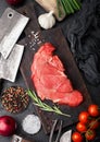 Fresh raw organic slice of braising steak fillet on chopping board with fork and knife on black stone background. Red onion, Royalty Free Stock Photo