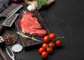 Fresh raw organic slice of braising steak fillet on chopping board with fork and knife on black stone background. Red onion, Royalty Free Stock Photo
