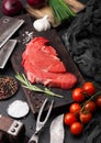 Fresh raw organic slice of braising steak fillet on chopping board with fork and knife on black stone background. Red onion, Royalty Free Stock Photo