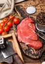 Fresh raw organic slice of braising steak fillet on chopping board with fork and knife on wooden background. Red onion, tomatoes Royalty Free Stock Photo