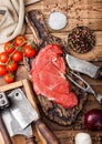 Fresh raw organic slice of braising steak fillet on chopping board with fork and knife on wooden background. Red onion, tomatoes Royalty Free Stock Photo