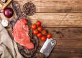 Fresh raw organic slice of braising steak fillet on chopping board with meat hatchet on wooden background. Red onion, tomatoes Royalty Free Stock Photo