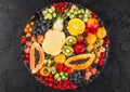 Fresh raw organic summer berries and exotic fruits in round large tray on black kitchen background. Papaya, grapes, nectarine, Royalty Free Stock Photo