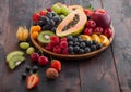 Fresh raw organic summer berries and exotic fruits in round wooden plate on dark wooden kitchen background. Papaya, grapes, Royalty Free Stock Photo