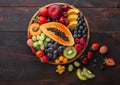 Fresh raw organic summer berries and exotic fruits in round wooden plate on dark wooden kitchen background. Papaya, grapes, Royalty Free Stock Photo