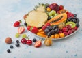 Fresh raw organic summer berries and exotic fruits in white plate on blue kitchen background. Pineapple, papaya, grapes, nectarine Royalty Free Stock Photo