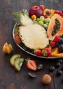 Fresh raw organic summer berries and exotic fruits in white plate on dark wooden background. Pineapple, papaya, grapes, nectarine Royalty Free Stock Photo